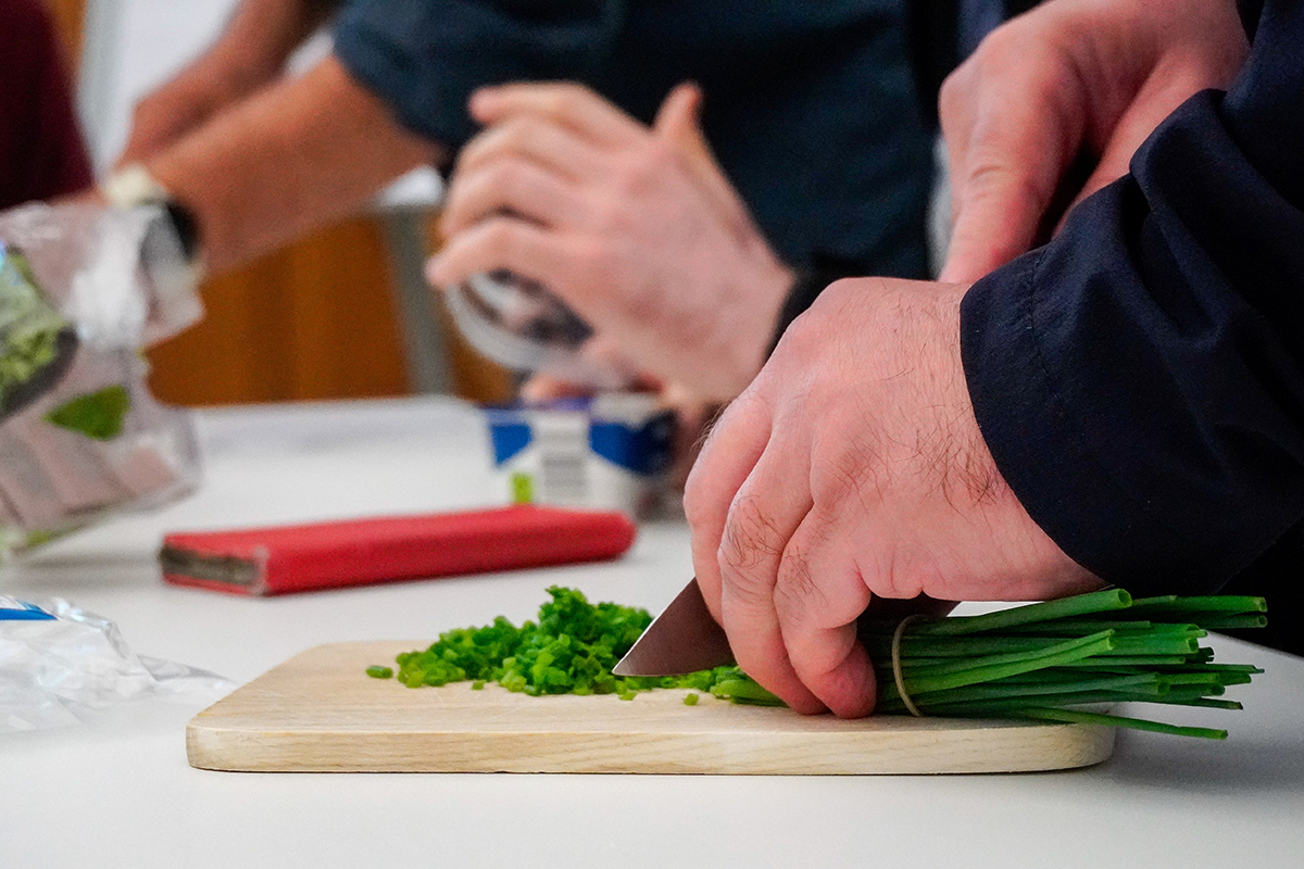 Fotografie - Hand schneidet frischen Schnittlauch auf einem Schneidebrett in der Küche.