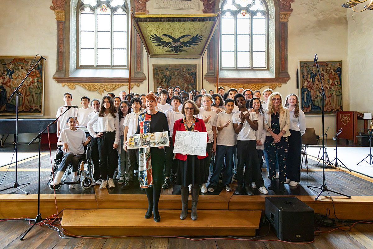 Fotografie - Das Ensemble des Collège La Charme aus Clermont-Ferrand und die Samba Bateria Feijoada der Clermont-Ferrand-Mittelschule zusammen mit der stellvertretenden Bürgermeisterin für Kultur, Isabelle Lavest, und Oberbürgermeisterin Gertrud Maltz-Schwarzfischer, die das von den Sketchers gestaltete jeweilige Jubiläumsgeschenk überreichten.