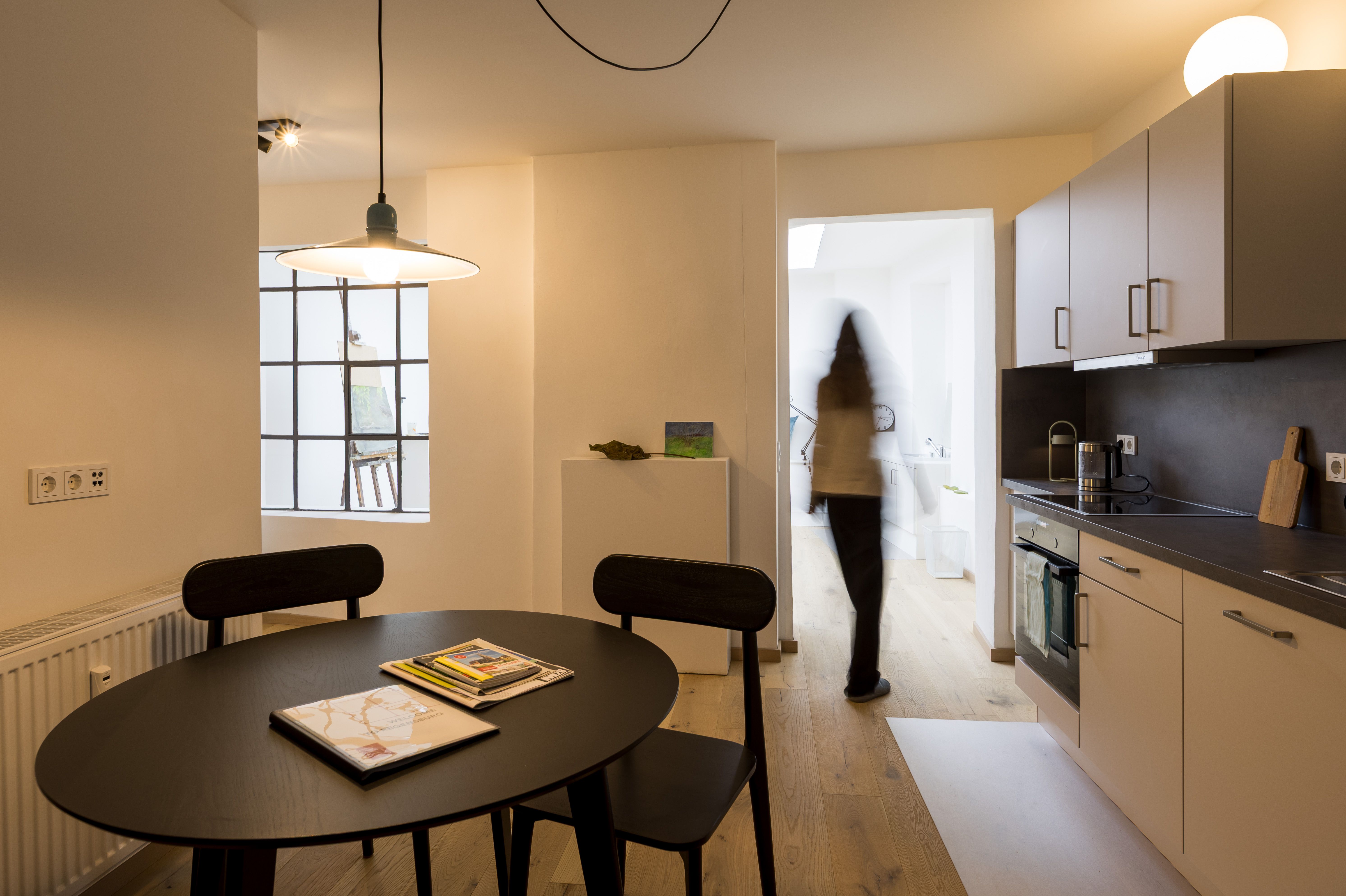 Fotografie - Atelierwohnung 1 - Die Abbildung zeigt eine verschwommene weibliche Silhouette, die gerade von der Küche in das Studio geht.