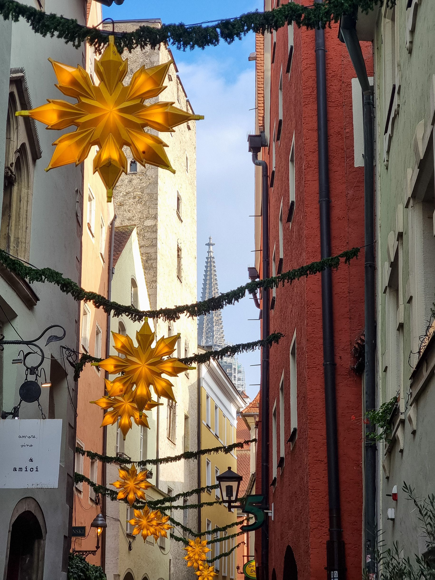 Fotografie: Girlanden aus Tannenzweigen mit je einem großen gelb beleuchteten Stern in der Mitte spannen sich über die Gasse „Hinter der Grieb“. Im Hintergrund sind die Spitzen der Domtürme zu sehen. 