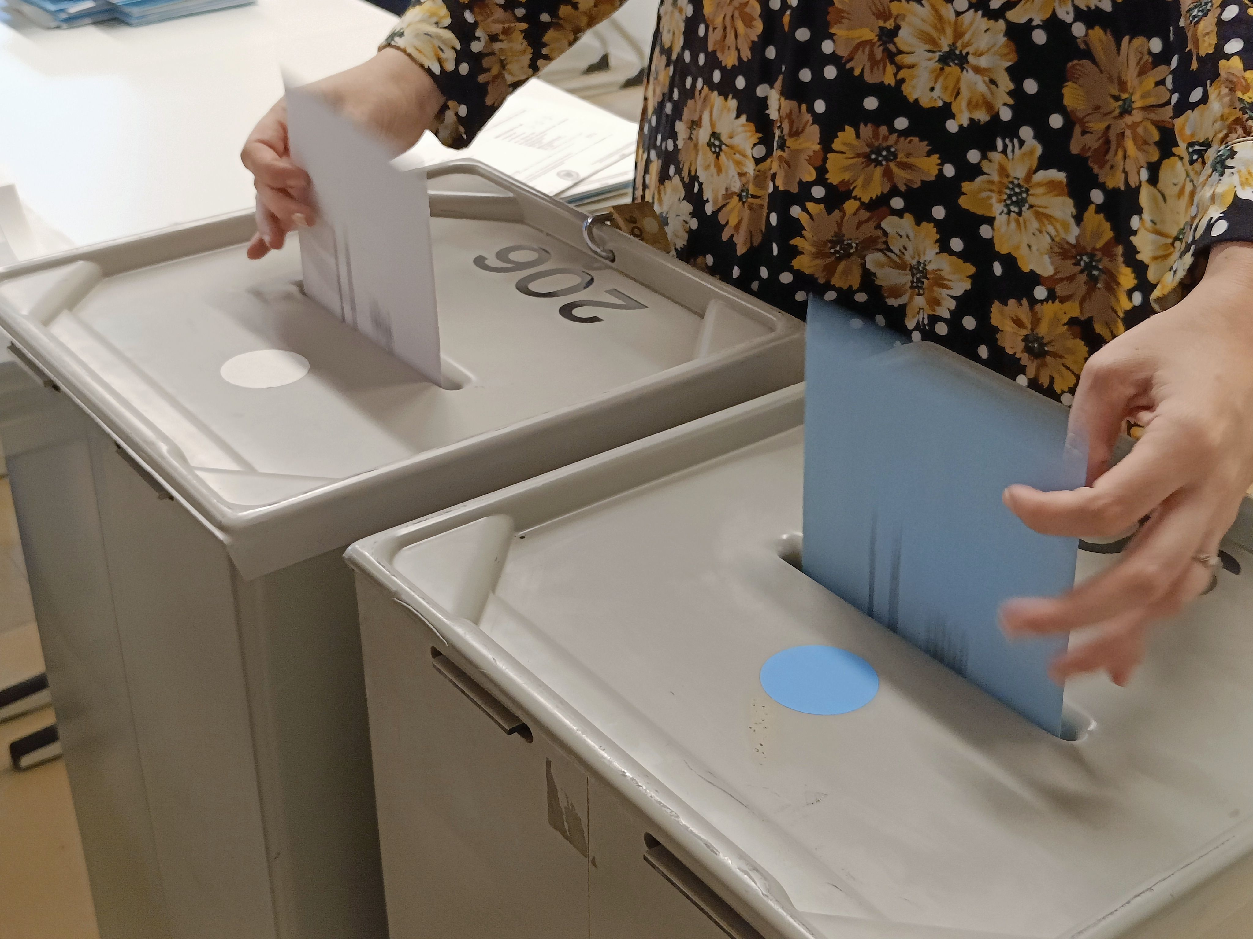 Fotografie: Eine Person wirft Umschläge in zwei Briefwahlurnen.