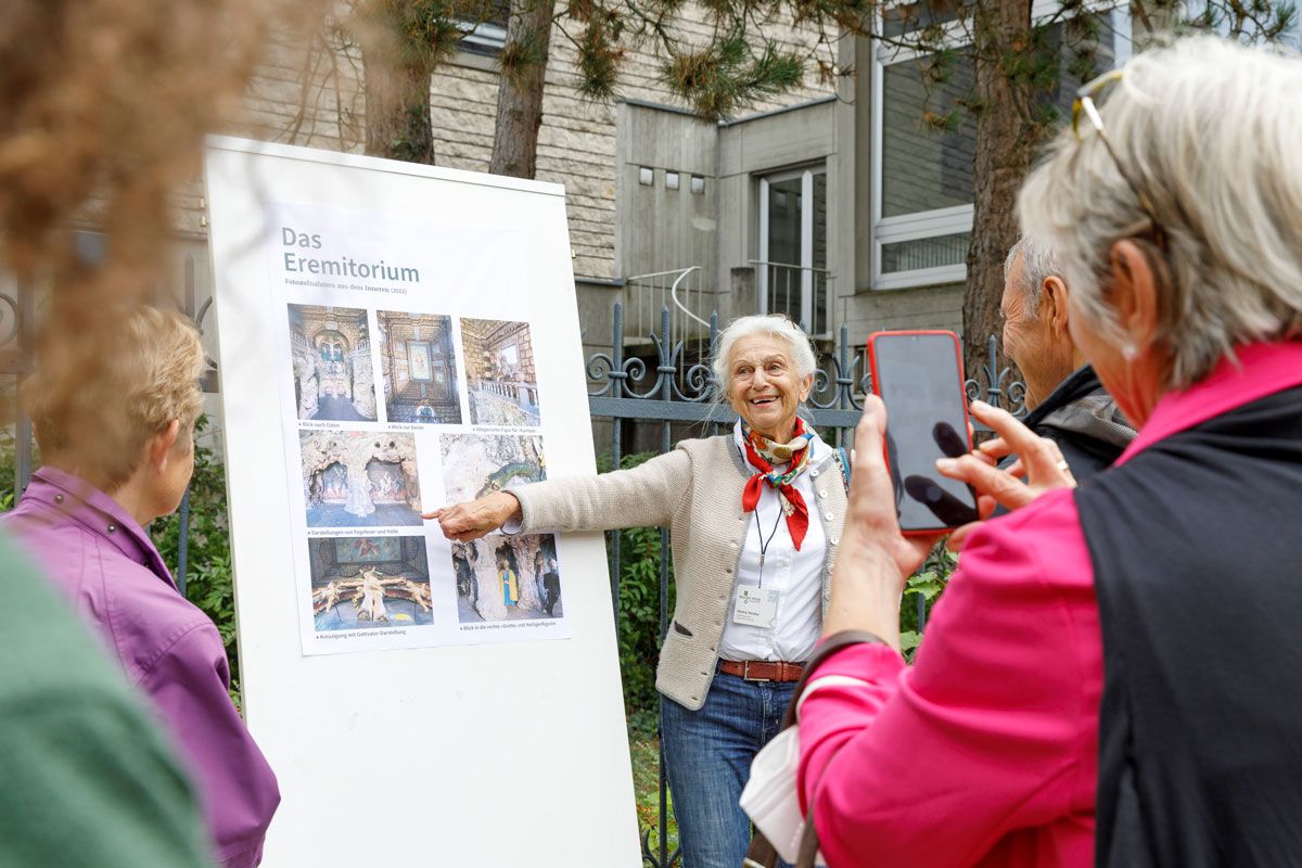 Fotografie: Eine Frau erklärt eine Denkmaltafel.