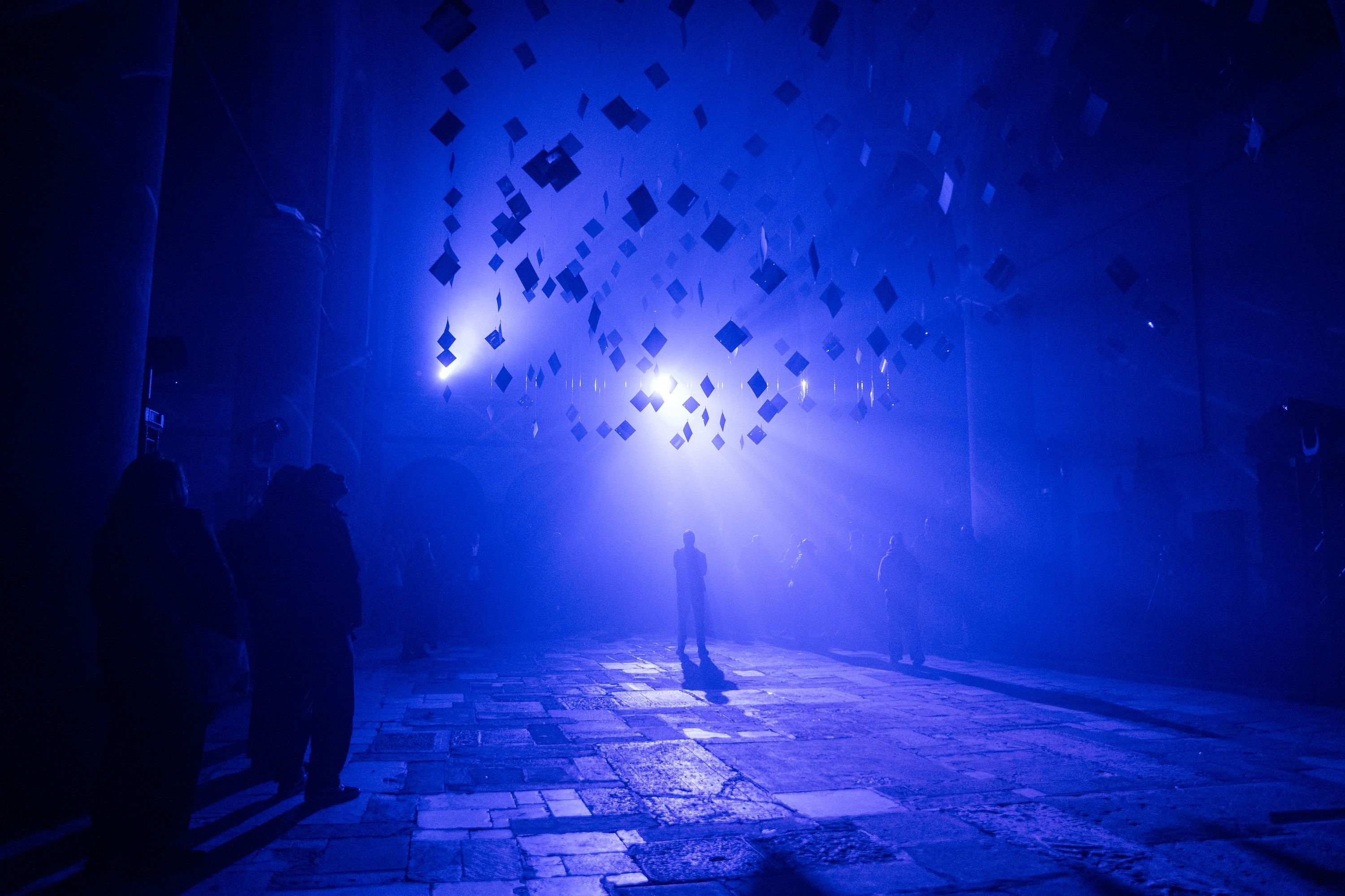 Fotografie – RE.LIGHT Onionlab, silberne Blättchen werden mit blauem Licht angestrahlt, darunter steht ein Mensch in hellem Licht