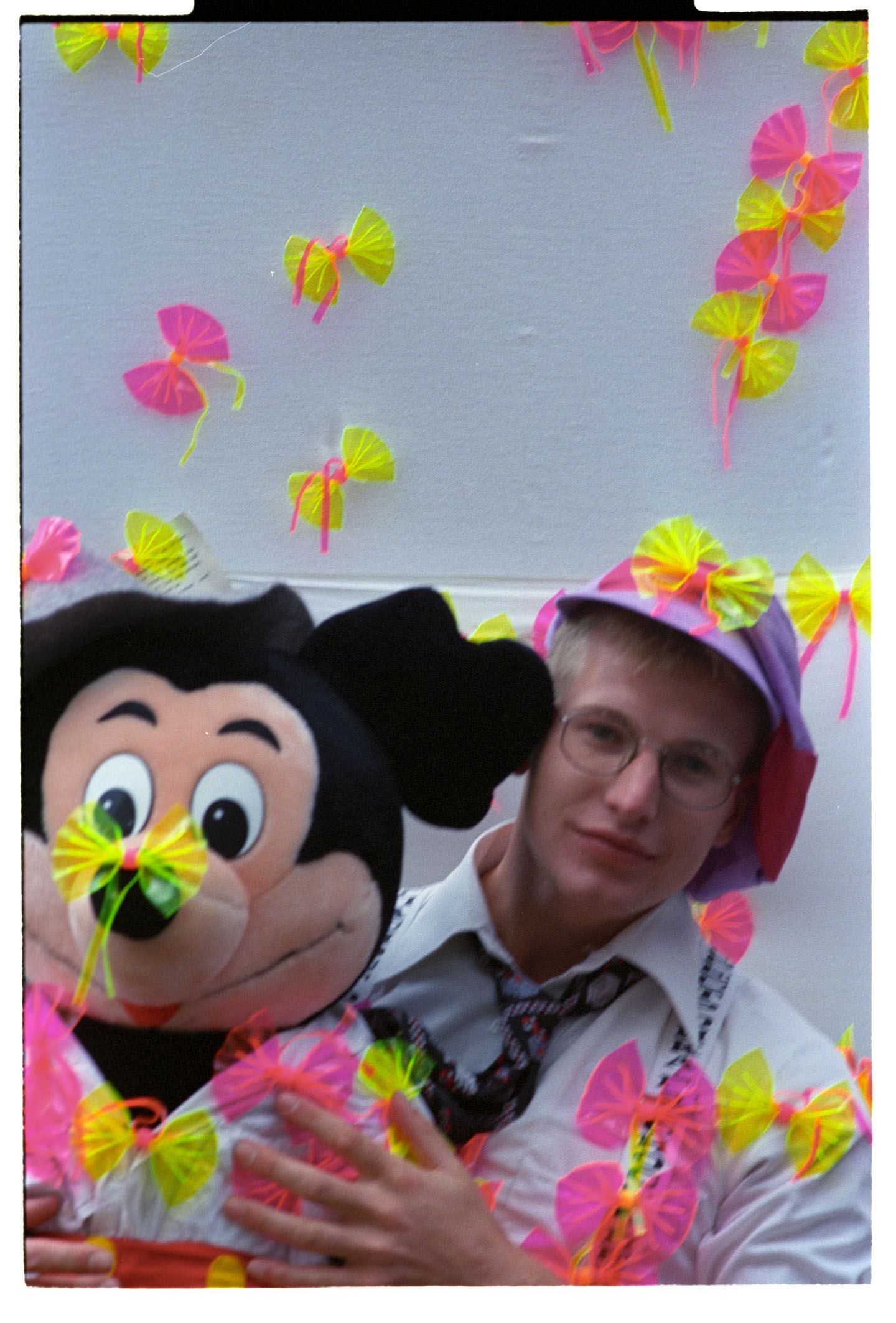 Fotografie: Ein junger Mann mit einer Micky-Maus-Plüschfigur und Plastikschleifen in der Umgebung