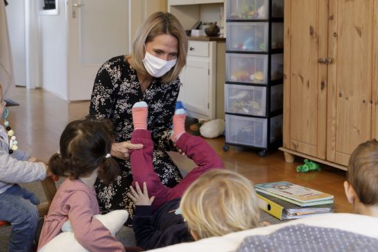 Fotografie – Tagesmutter spielt mit Kindern in Wohnzimmer