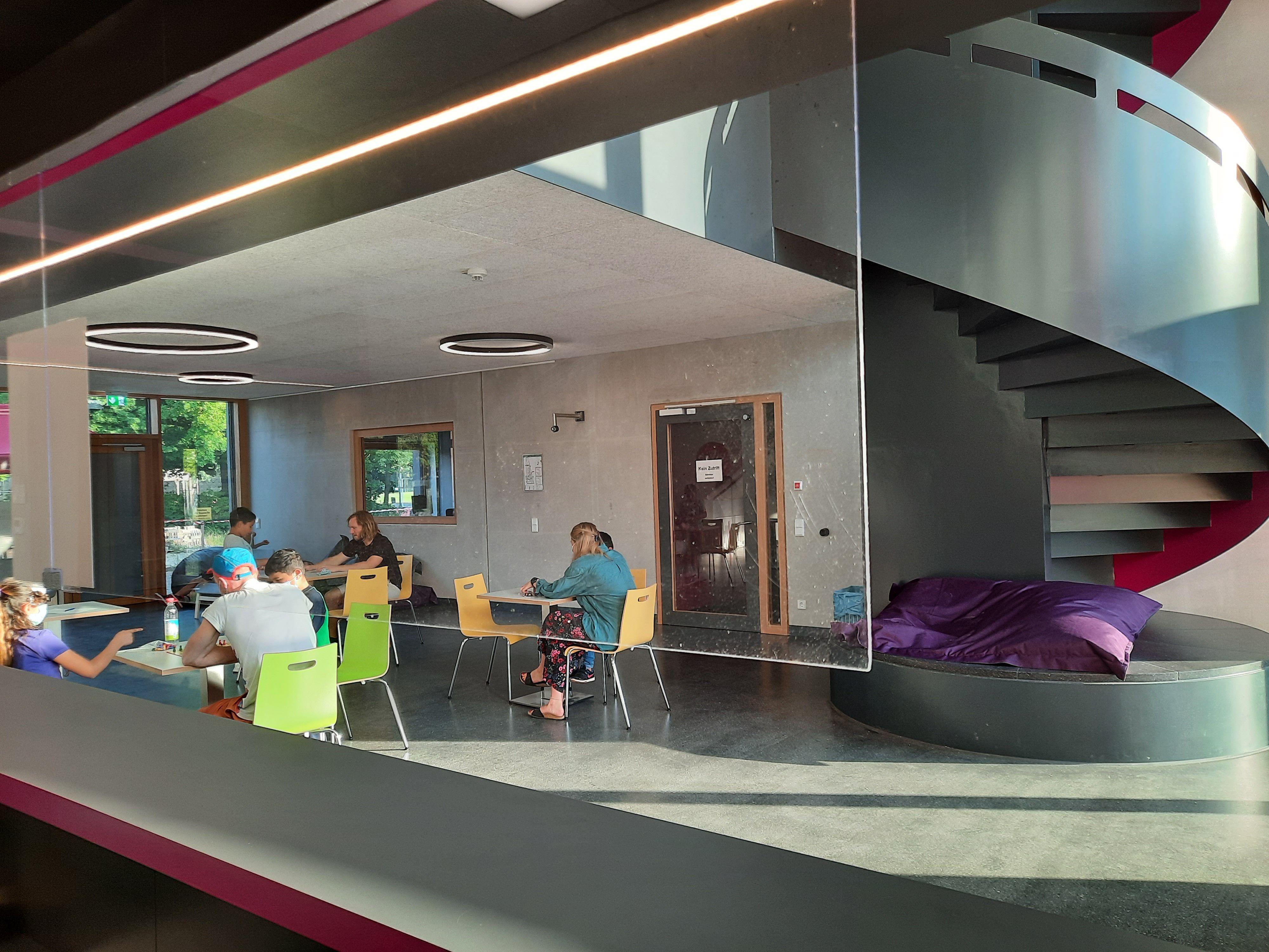 Es ist das Foyer des Jugendzentrums mit Personen zu sehen, welche an Tischen Gesellschaftsspiele spielen.