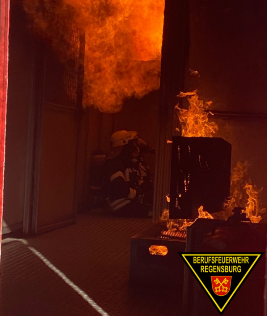 Fotografie: Einsatzkräfte der Feuerwehr sitzen am Boden eines Containers, über ihnen sind Flammen sichtbar.