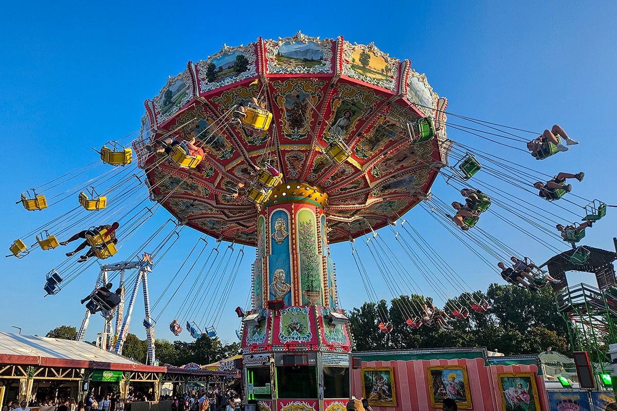 Fotografie - Buntes Kettenkarussell in voller Fahrt auf der Regensburger Dult, mit schwingenden Gondeln vor klarem Himmel.