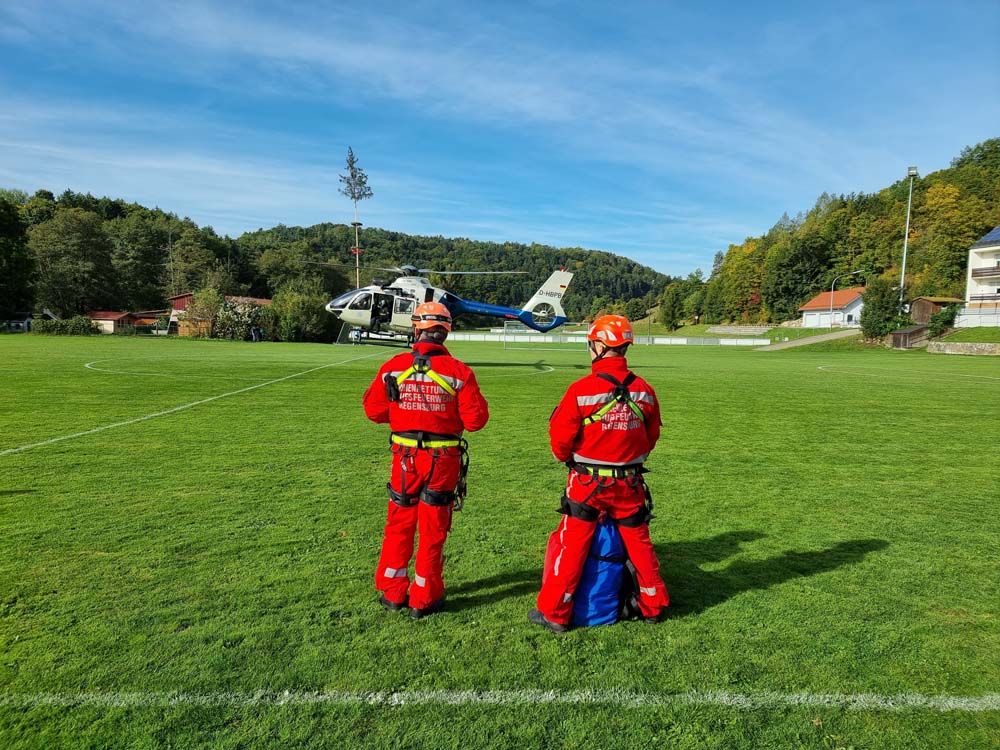Fotografie: Höhenretter warten auf einen landenden Hubschrauber auf einem Sportplatz.