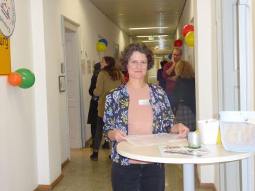 Mitarbeiterin am Stehtisch, im Hintergrund Besucher am Tag der offenen Tür
