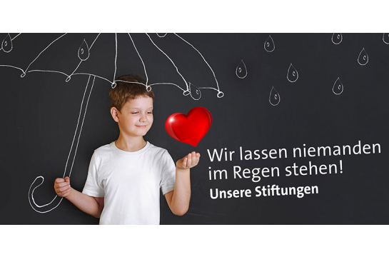 Themenbild Städtische Stiftungen - Symbolbild - kleiner Junge steht vor einer Tafel, auf der ein Regenschirm und Regentropfen gemalt sind und ein rotes Herz schwebt über seiner linken Hand