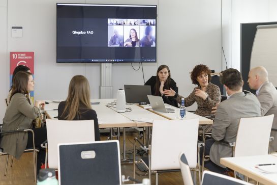 Fotografie: Eine Arbeitsgruppe sitzt an einem Tisch, während Qingdao hybrid zugeschalten wird.