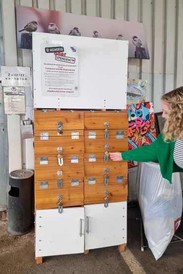 Fotografie: Sabine Obermeier vor den absperrbaren Fächern der Annahmestelle für gebrauchte Laptops auf dem Recyclinghof