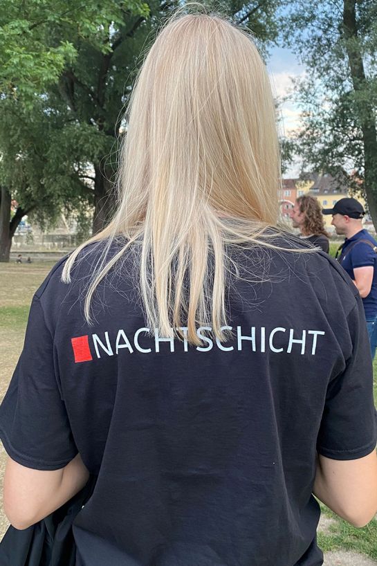 Fotografie - junger Mensch mit dem Rücken zur Kamera mit einem dunkelblauen T-Shirt, auf dem „Nachtschicht“ steht (C) Stefan Adler, Stadt Regensburg