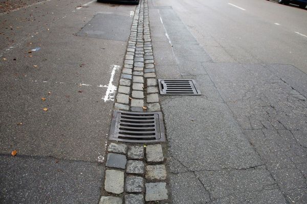 Prüfeninger Straße - Fotografie - 3-zeilige Rinne aus Granitgroßsteinen und Gullydeckel sowie schadhafter Fahrbahnbereich