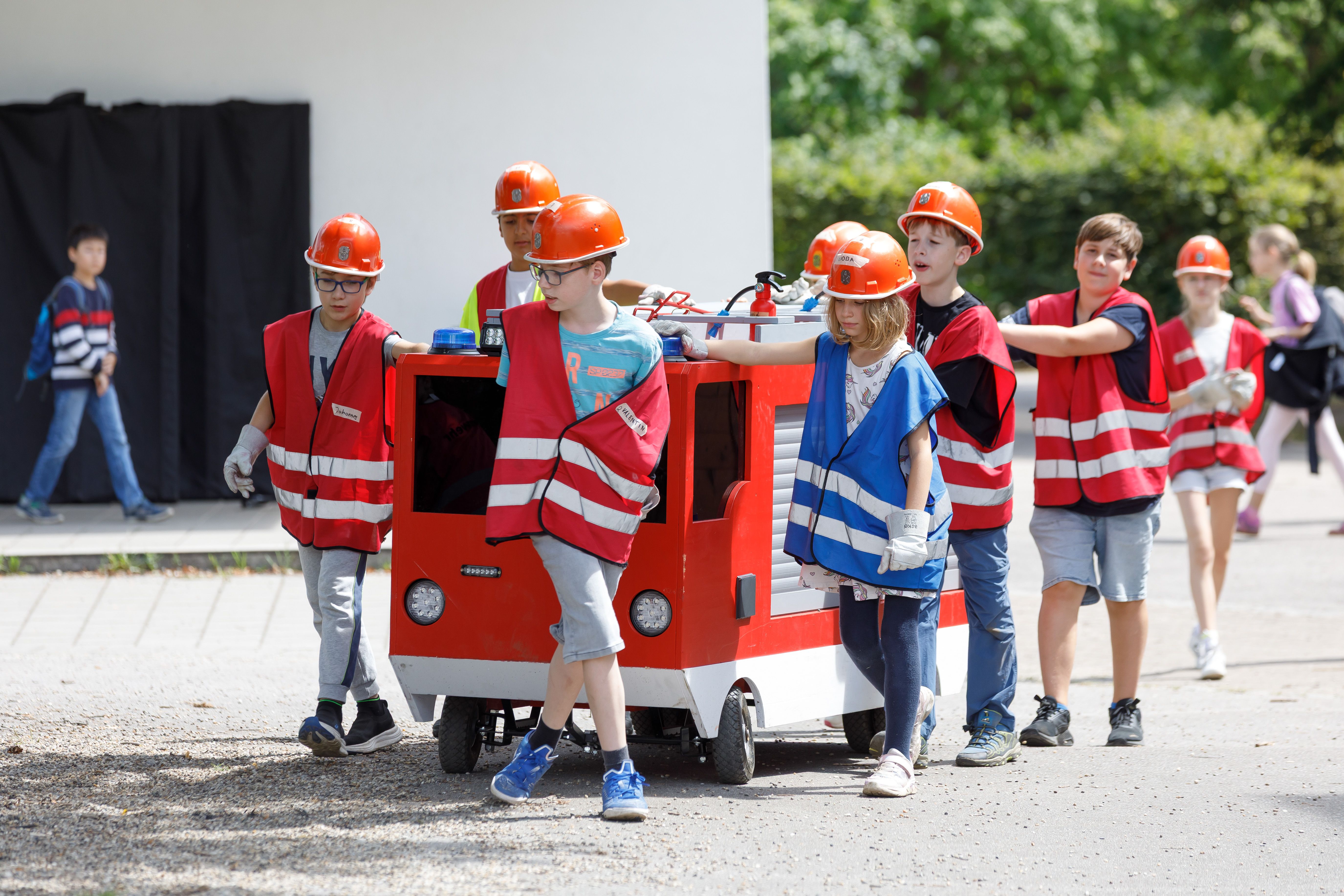 Fotografie: Die Mini-Feuerwehr schiebt ein kleines Feuerwehrauto.