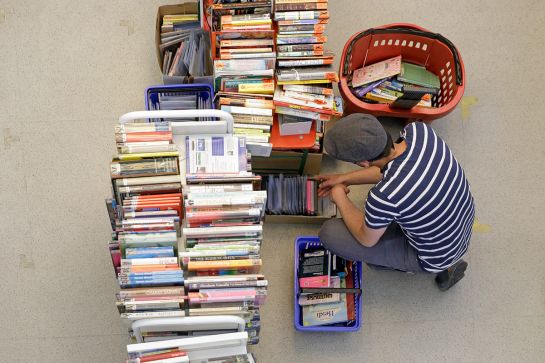 Foto von oben auf 2 Buchwägen voll Flohmarktware und eine Person, die Angebot durchsucht