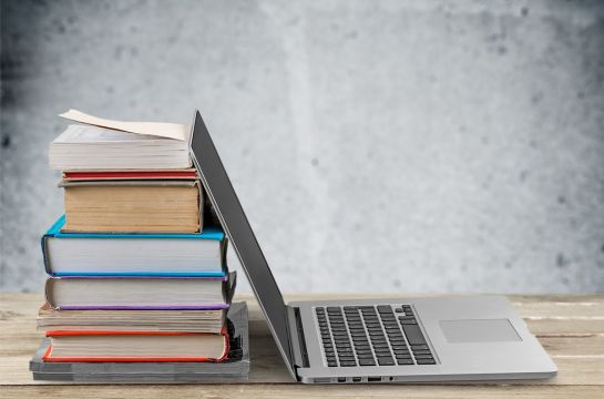 Fotografie - ein Laptop steht an einen Stapel Bücher gelehnt