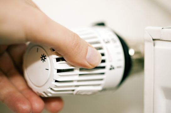 Fotografie: Eine Hand bedient ein Thermostat einer Heizung.