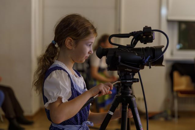 Mädchen im Dirndl schaut durch eine Filmkamera